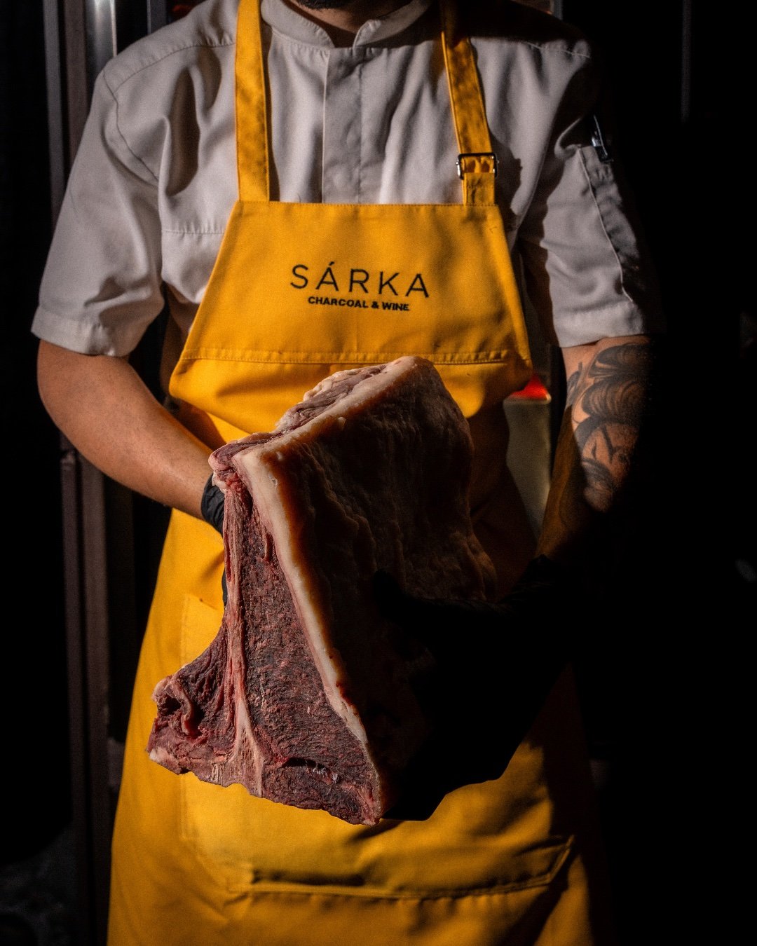 Chef in a SÁRKA apron holding a dry-aged cut