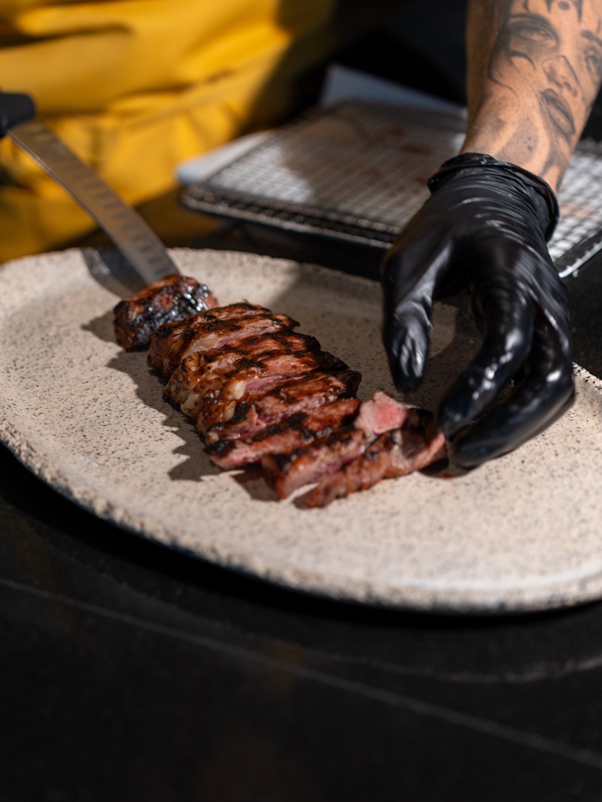 Gloved hands slicing a grilled steak on a stone plate